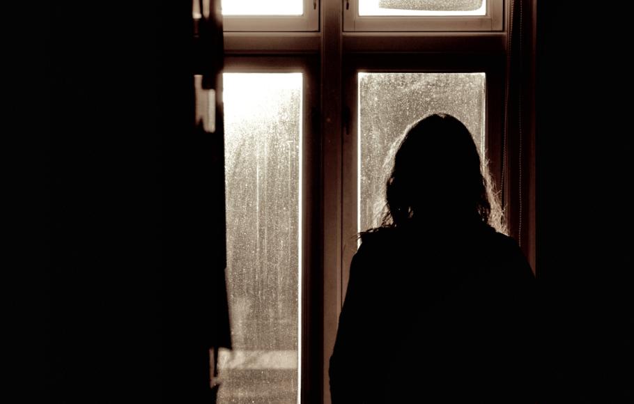 Kvinna står vid fönstret i mörkret